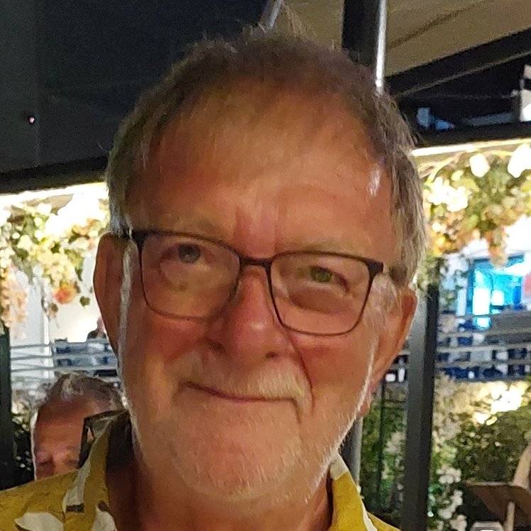A white, bearded man wearing glasses smiling at the camera with view of terraced bar behind